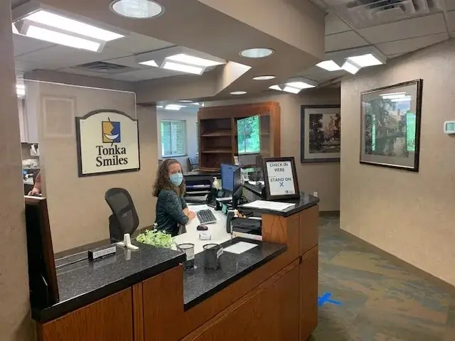 A team member at the Tonka Smiles reception counter, with the practice's sign on the wall.
